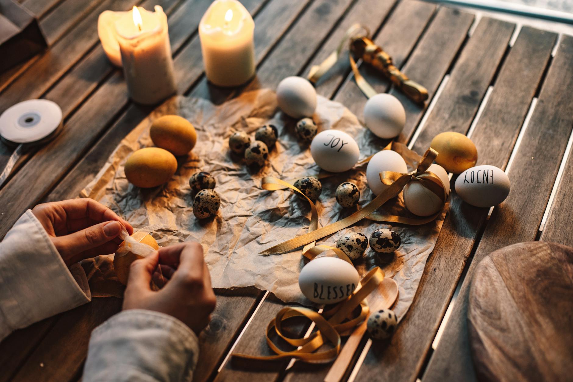 Świeczki, wstążki i pisanki ułożone na drewnianym stole