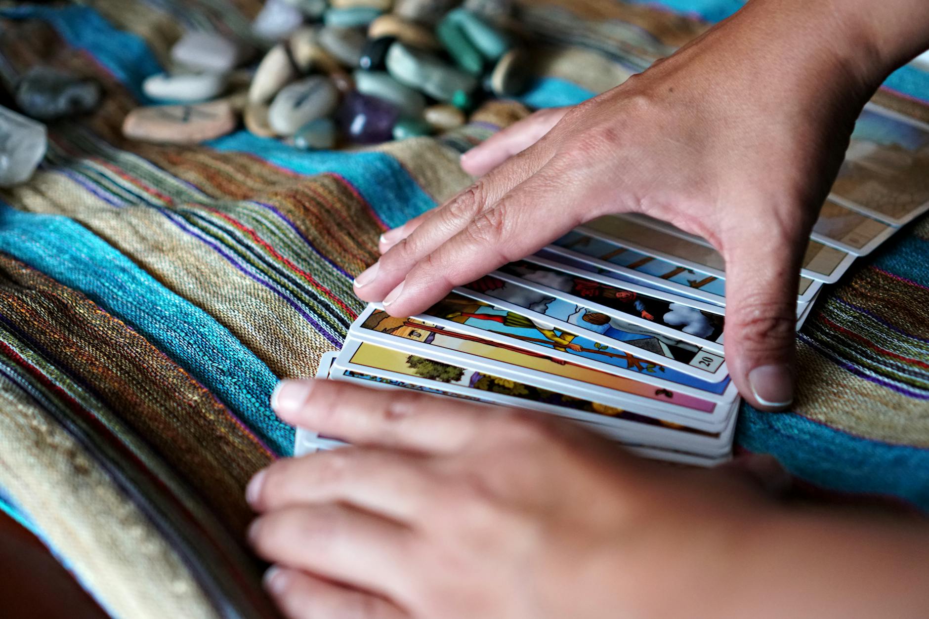 Dłonie układają karty tarota na kolorowej chuście z kamieniami