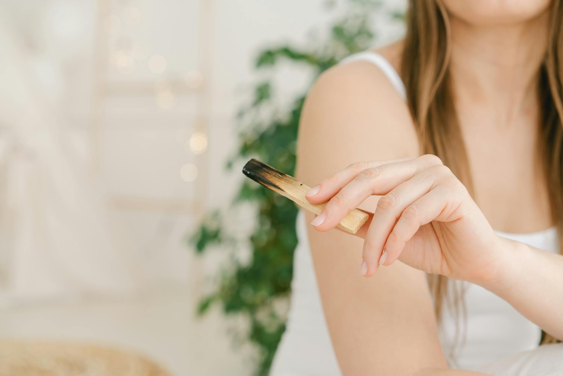 Kobieta w spokojnym wnętrzu trzymająca palo santo podczas medytacji