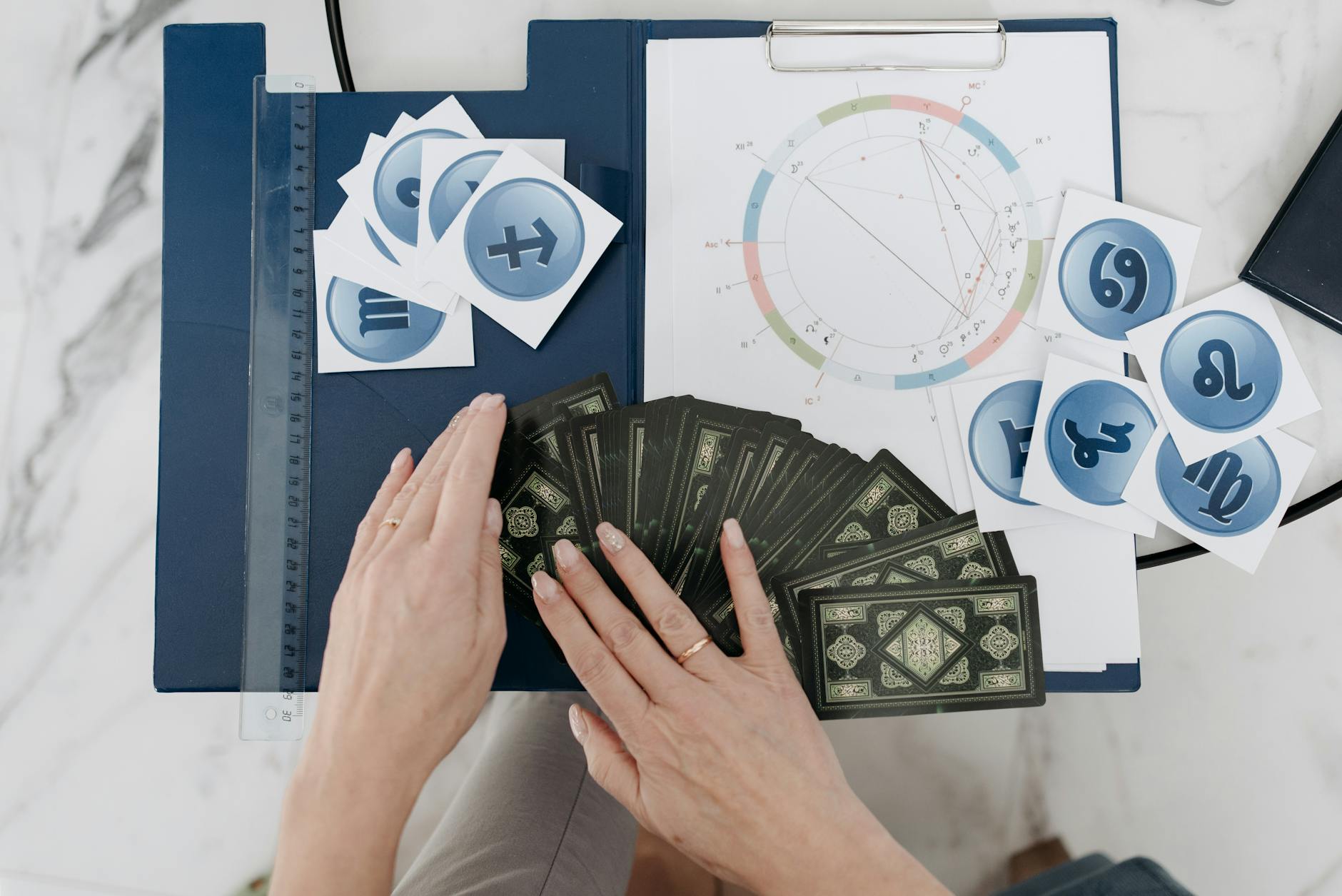 Dłonie układają karty tarota z symbolami astrologicznymi na stole